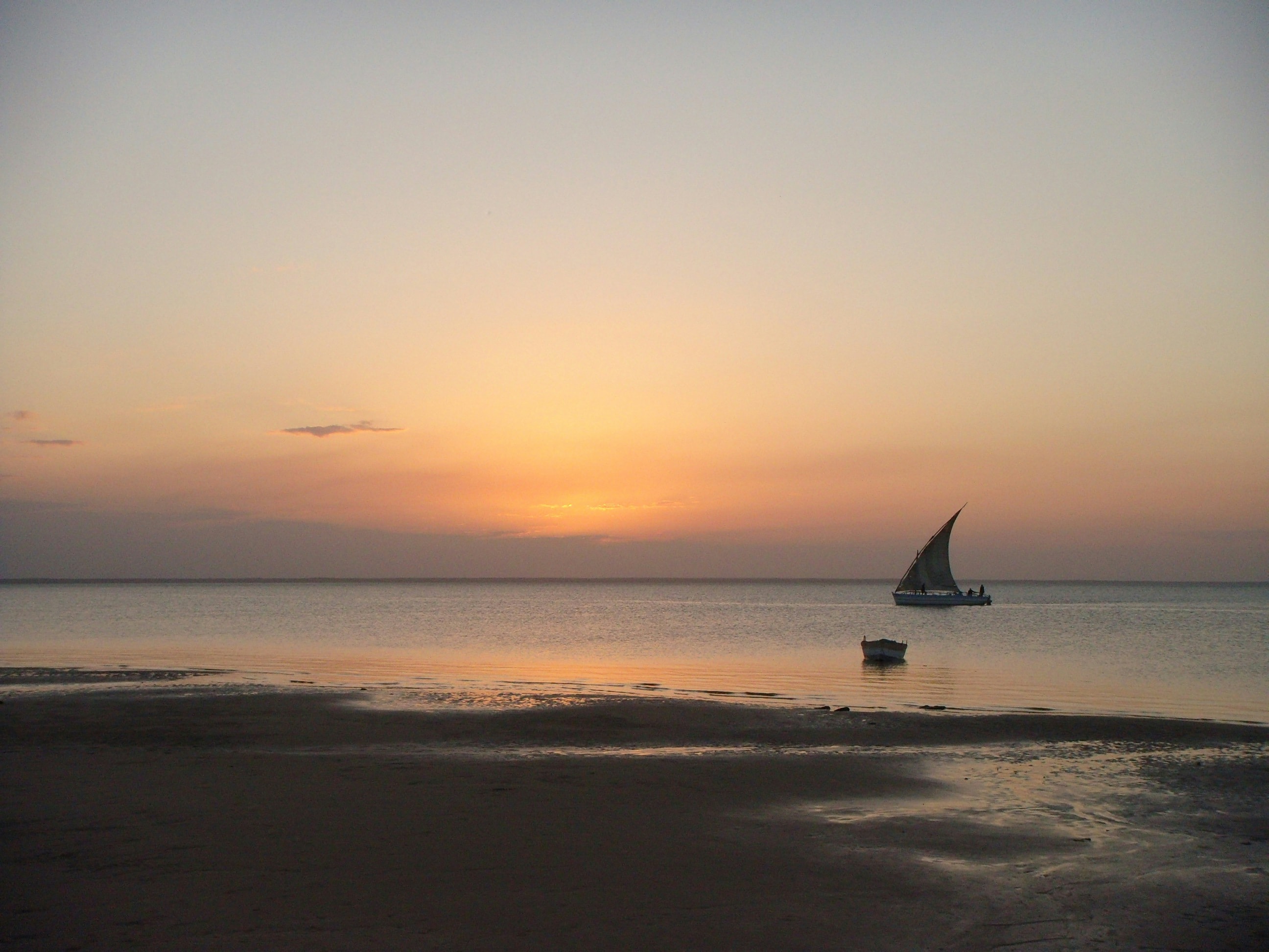 A lone dhow sailing on still water at sunset