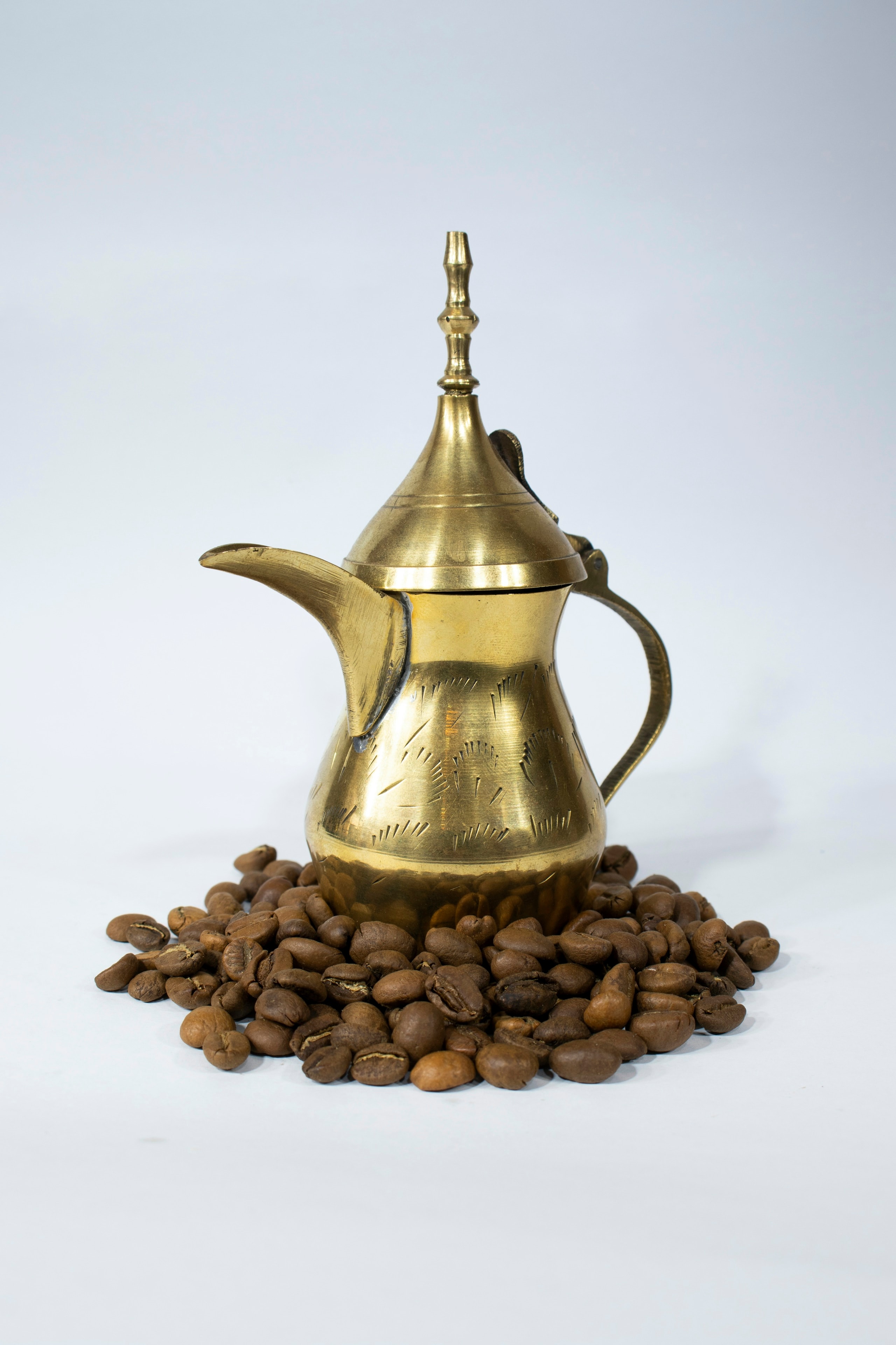 A brass Arabic coffee pot on a bed of roasted coffee beans